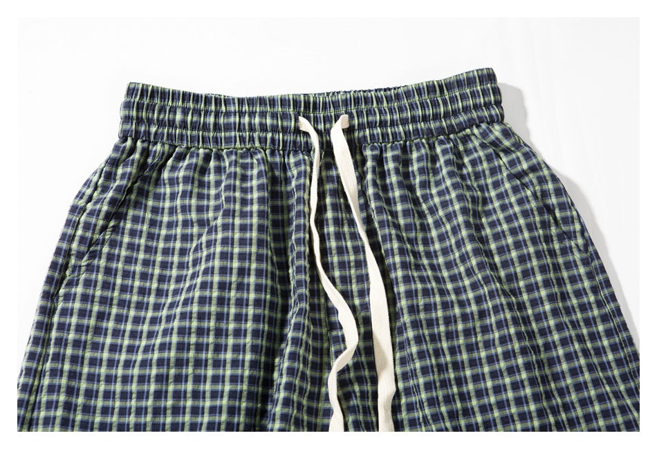 Front close-up of navy shorts with a green and blue plaid pattern, elastic waistband, and white drawstring.