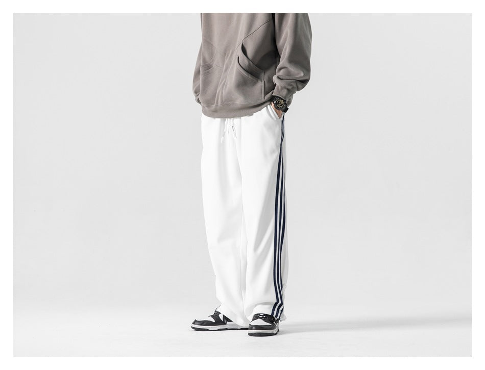 Cropped model wearing loose white track pants with dark side stripes, paired with a gray sweatshirt.