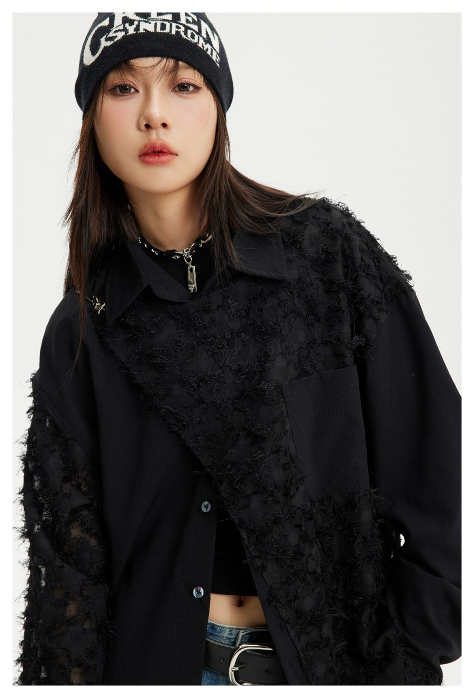 Close view of a model wearing an oversized black shirt with textured sheer panels, a chest pocket and button front.