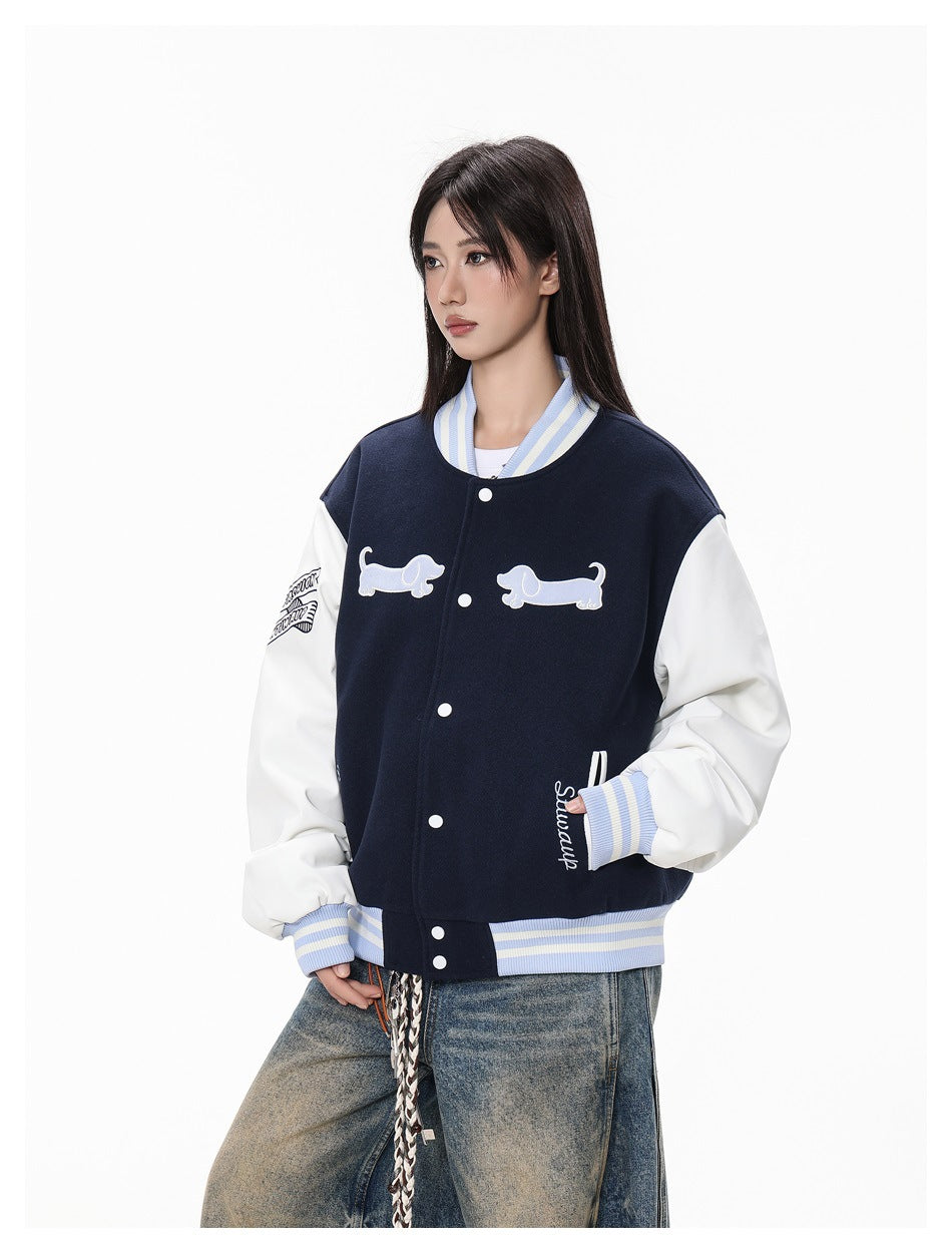 Model wearing a navy varsity jacket with white sleeves, striped blue-and-cream ribbing, snap buttons and dog appliqués.