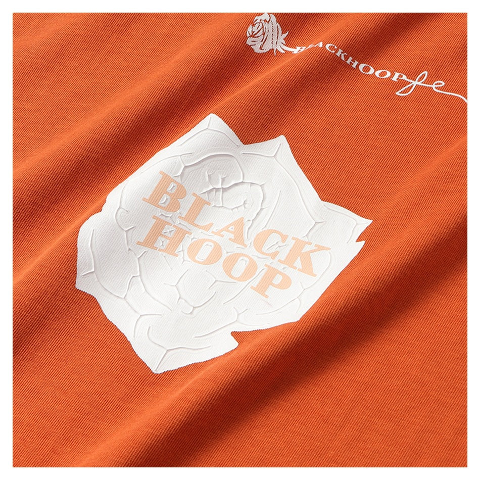 Close-up of an orange garment showing a raised white rose graphic and pale “BLACK HOOP” lettering.
