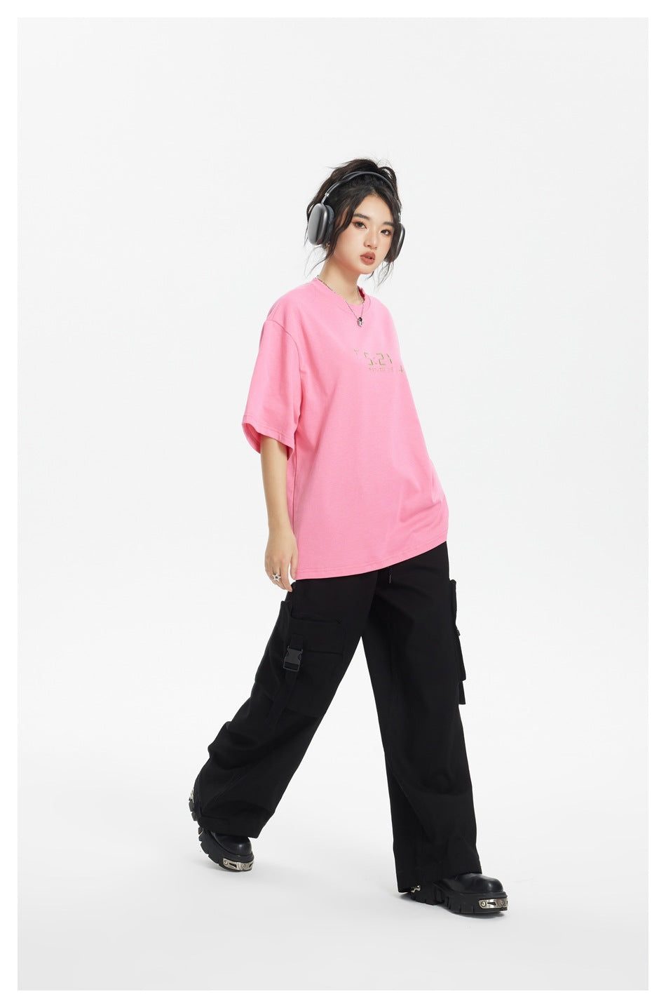 Full-length model wearing a bright pink oversized T-shirt, black cargo pants, and chunky black shoes.