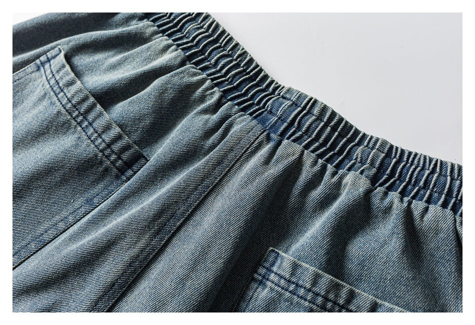 Close-up of blue denim trousers with a gathered elastic waistband and pocket seams.