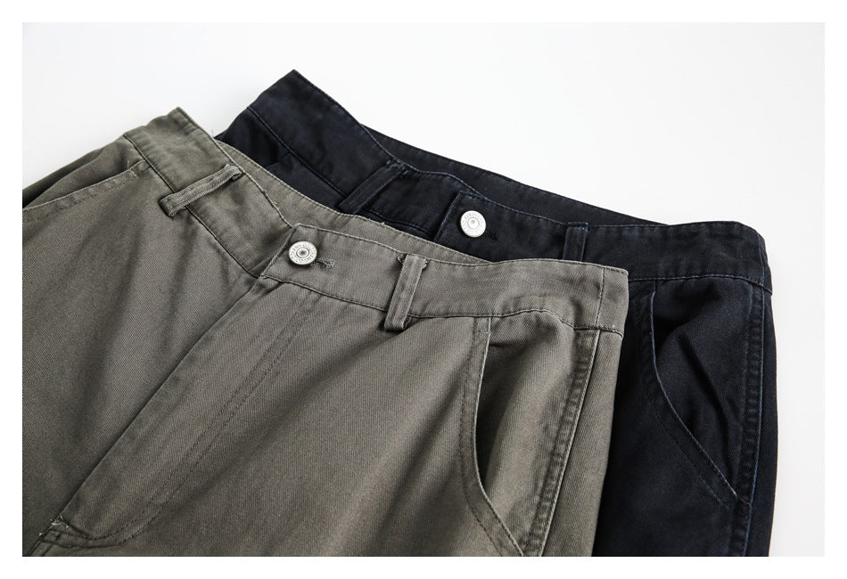Close-up of olive-gray and black pants overlapping, showing the waistbands, buttons, belt loops, and front pockets.