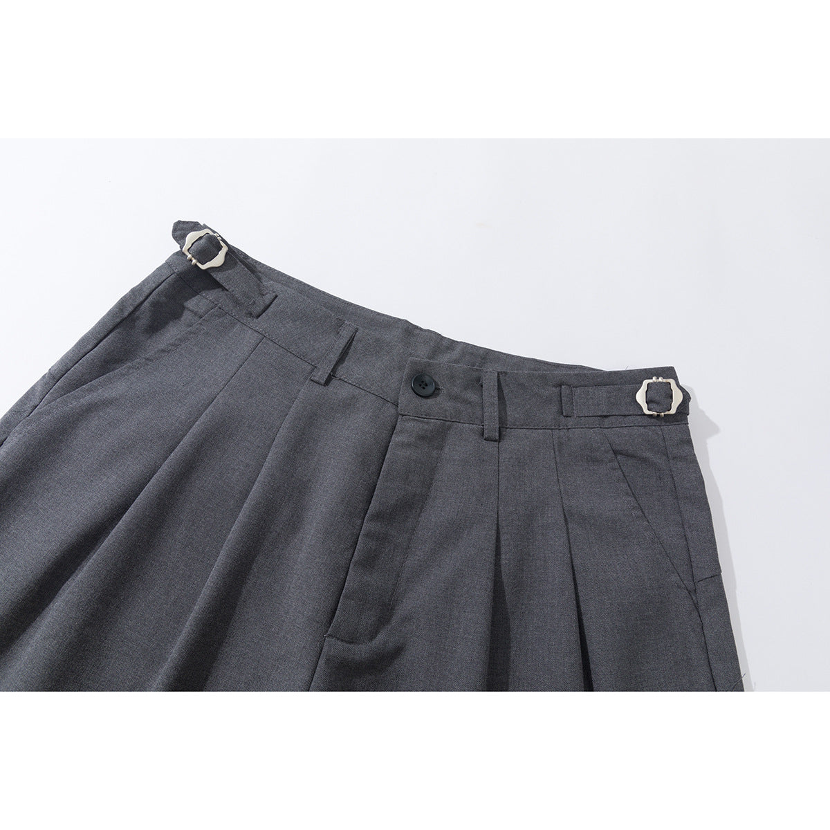Close-up of charcoal gray trousers showing pleats, a button, belt loops, and buckle side adjusters.