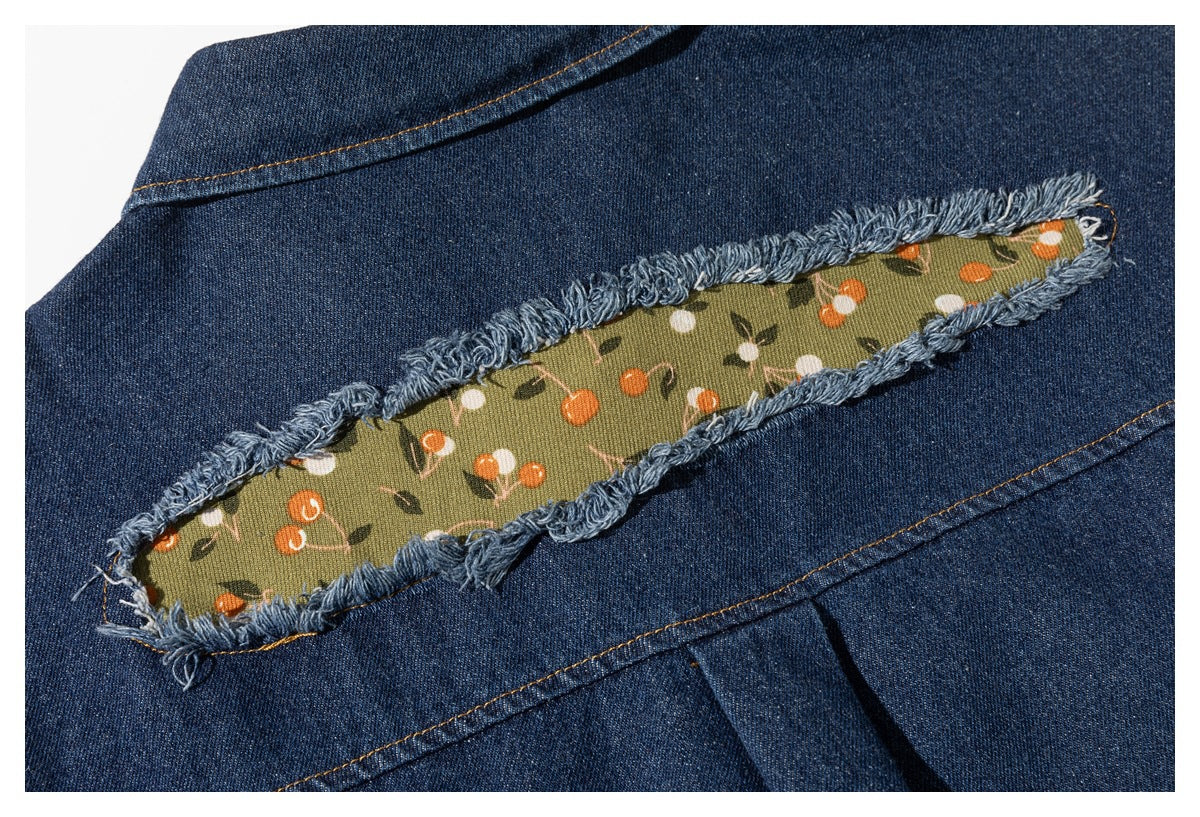 Close-up of dark blue denim with a frayed slit revealing olive fabric printed with small orange and white flowers.
