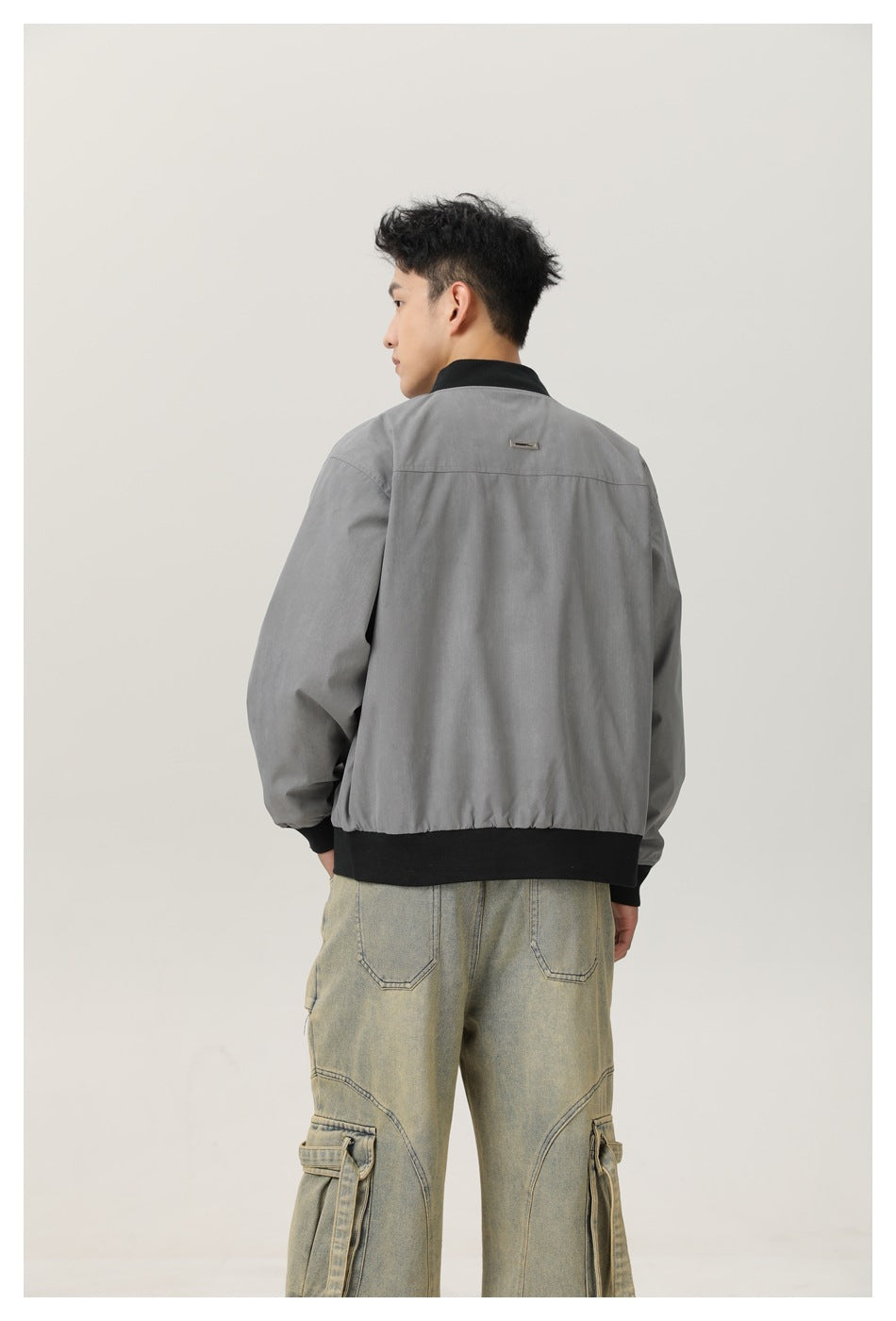Back view of a model wearing a gray bomber jacket with a black ribbed collar and hem.