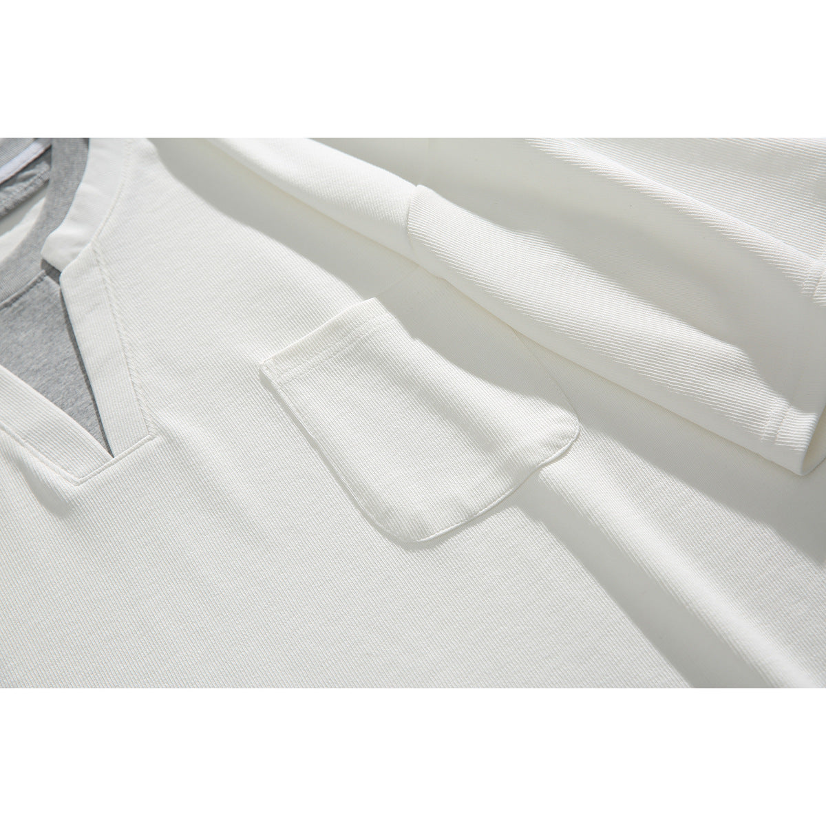 Close-up of a white ribbed shirt showing its chest pocket, short sleeve, and notched neckline.