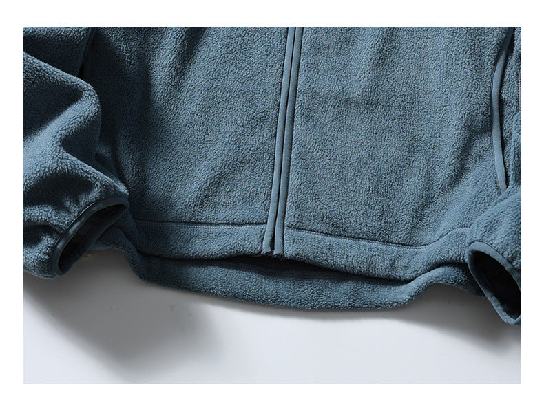Close-up of the blue-gray jacket's lower front, showing the zipper, hem stitching and sleeve cuffs.