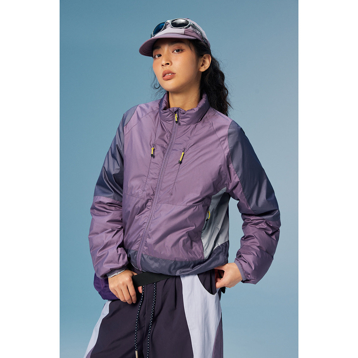 Woman wearing a purple and navy color-block zip jacket with high collar and yellow zipper pulls.