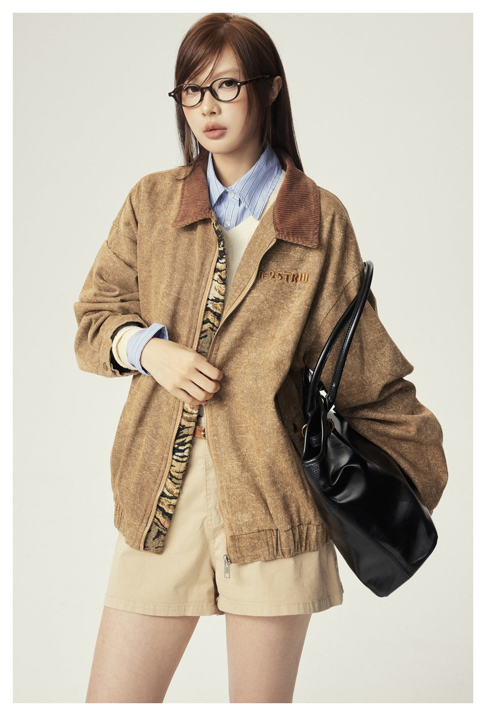 Close view of a model wearing a tan jacket with a brown collar and embroidered chest lettering.