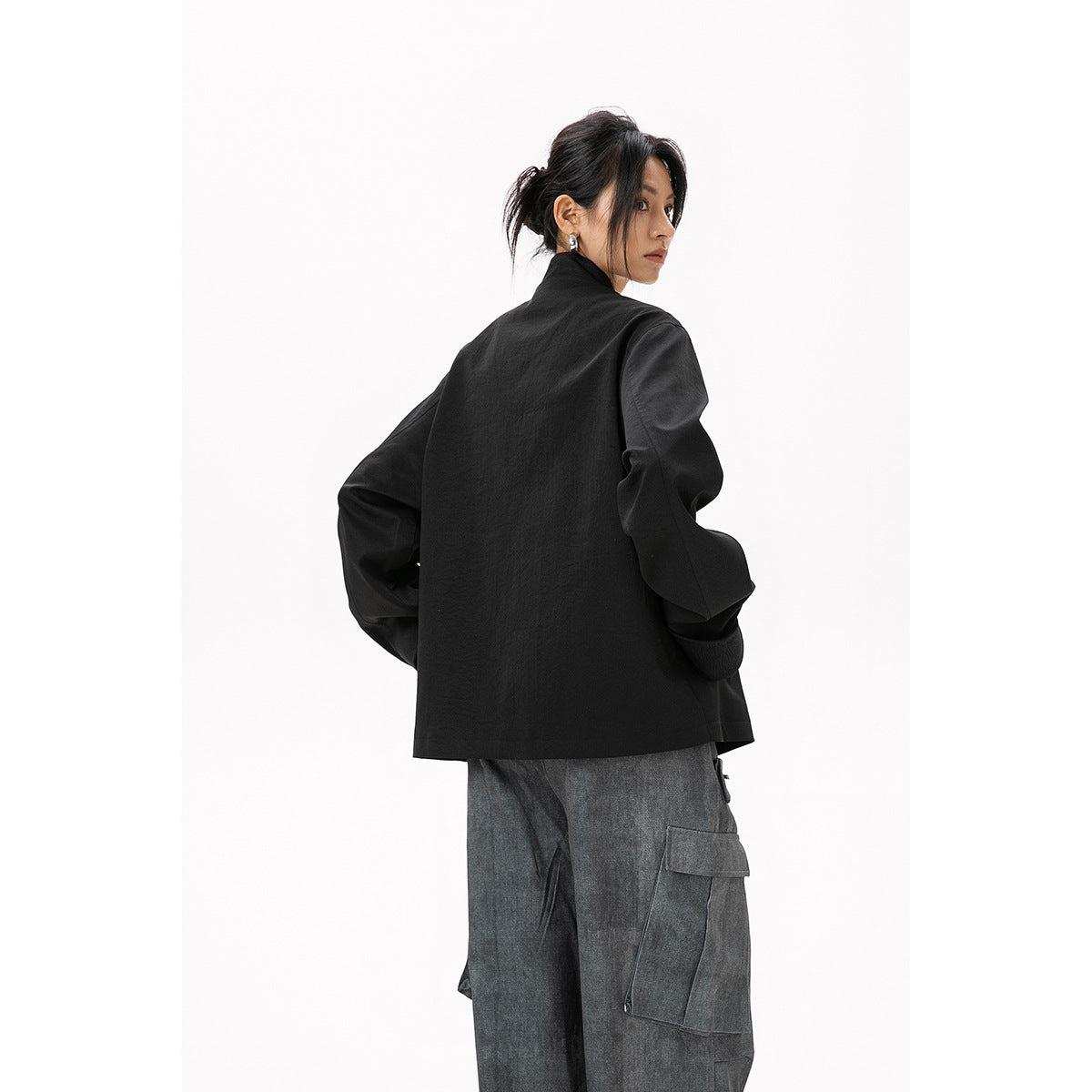 Rear three-quarter view of a model wearing a black jacket with loose gray cargo pants.