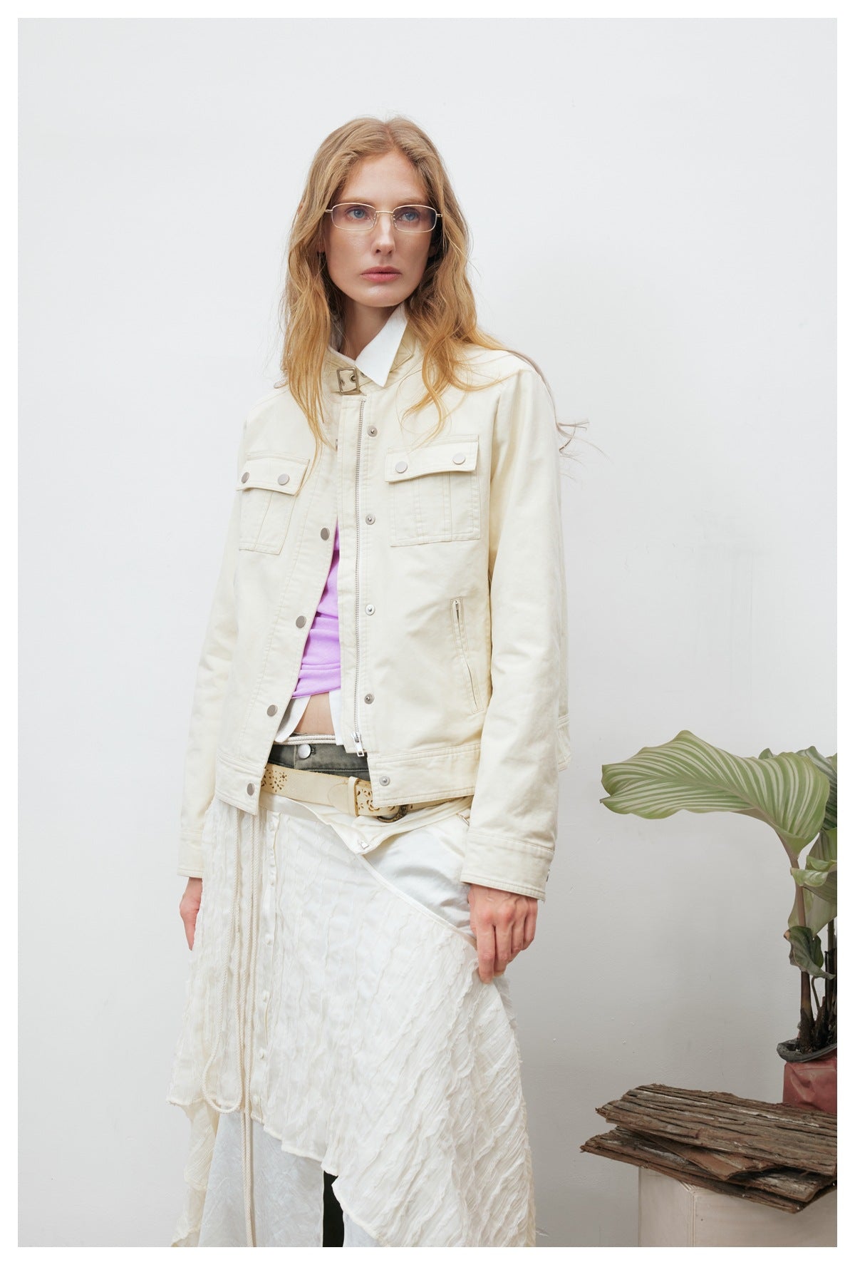 Model wearing an ivory snap-front jacket with flap pockets over a lilac top and white layered skirt.