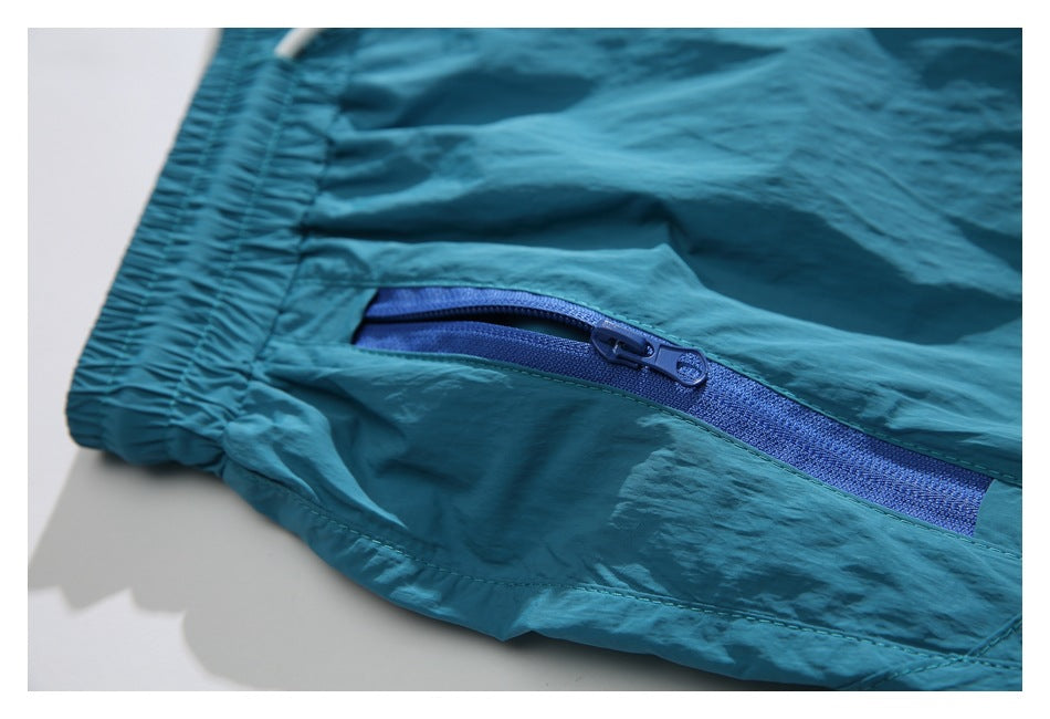 Close-up of teal shorts showing an elastic edge and a blue zippered pocket.
