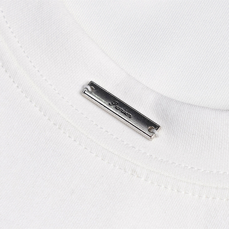 Close-up of a small silver metal label attached beside the white T-shirt's stitched crew neckline.