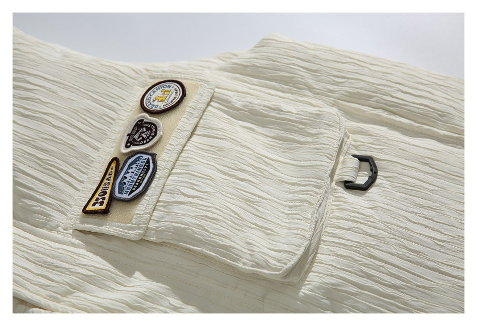 Close-up of an ivory vest pocket, textured fabric, decorative badges, and a small black side loop.