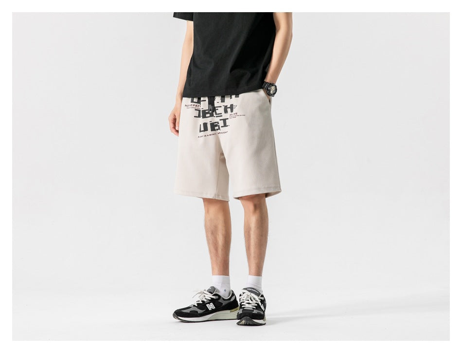 Front view of a model wearing light beige knee-length shorts with a black and red graphic.
