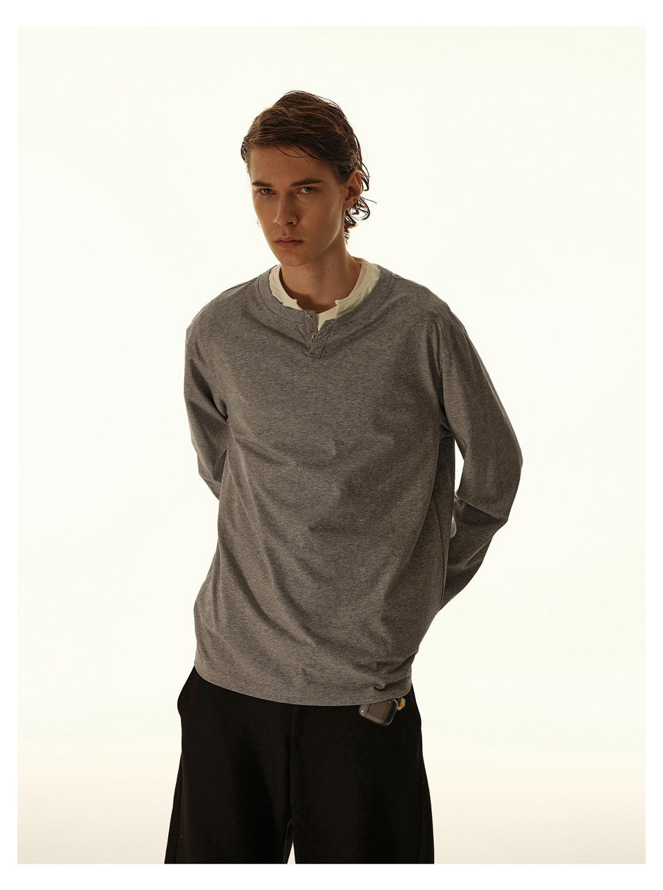 Closer view of a model wearing a gray long-sleeve henley with a short button placket over a white shirt.