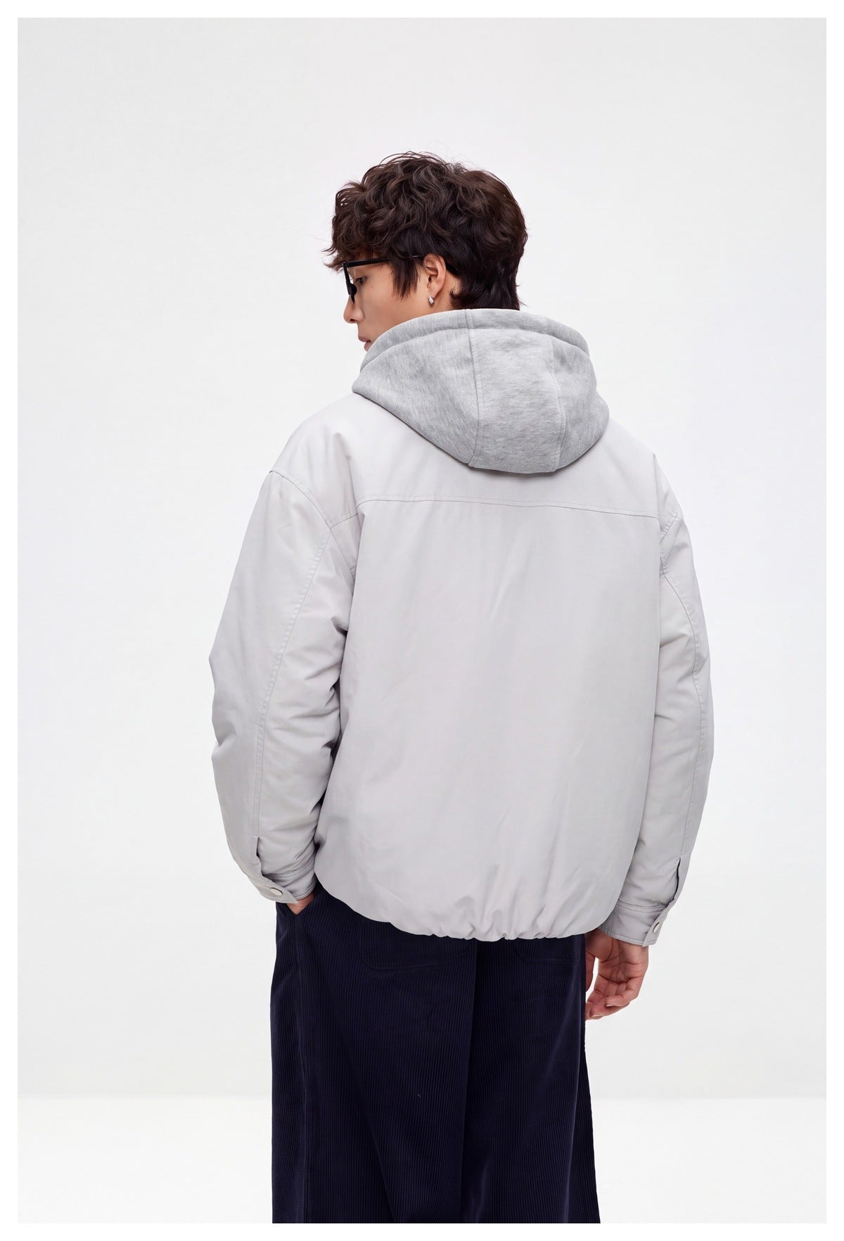 Back view of a model wearing a light gray jacket with a gray hood and gathered hem.