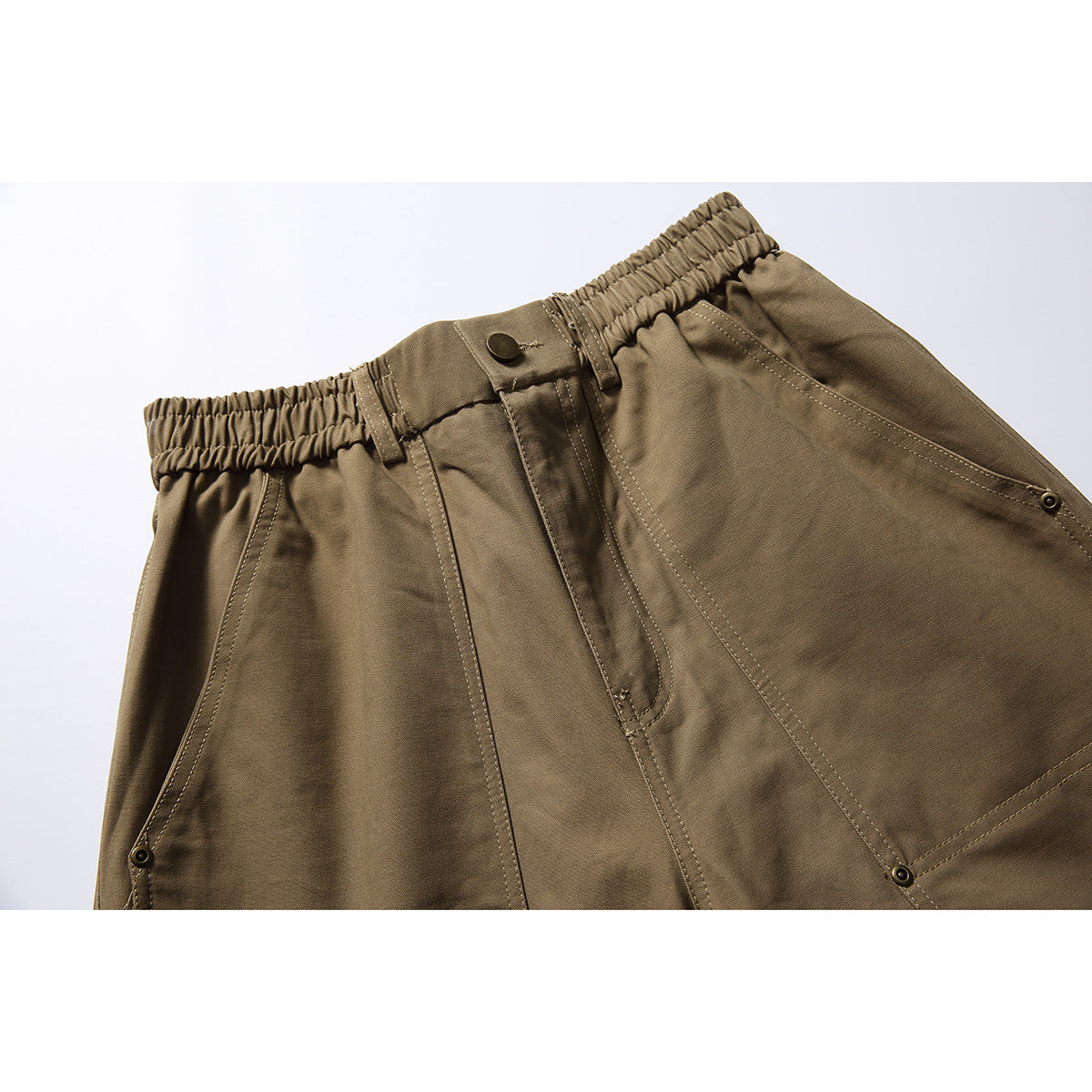 Close-up of olive-brown trousers showing an elastic waistband, button fly, and stitched front pockets.