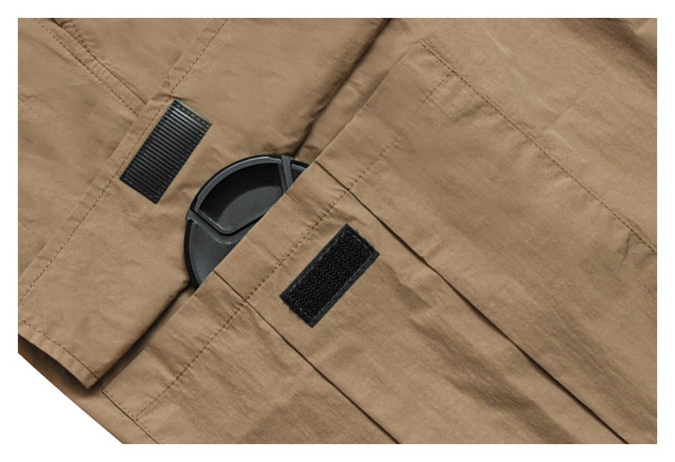 Close-up of tan garment fabric with a flap pocket, black hook-and-loop patches, and a plastic fitting.