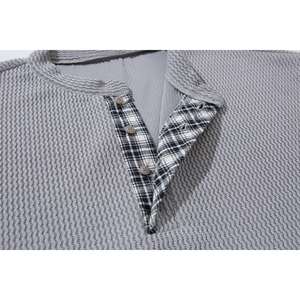 Close-up of a light gray textured pullover's round neckline and button placket with black-and-white plaid trim.