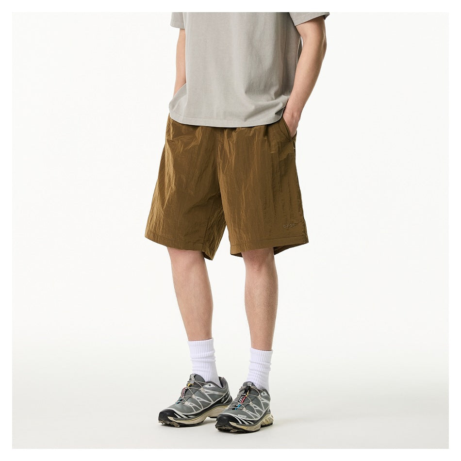 Front view of a model wearing loose olive-brown knee-length shorts with a drawstring and pockets.