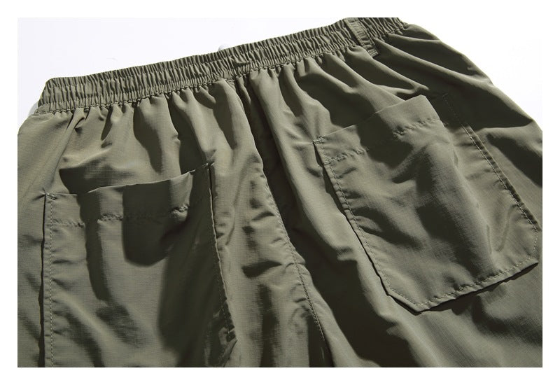 Close-up of olive-gray shorts with an elastic waistband and two large rear patch pockets.