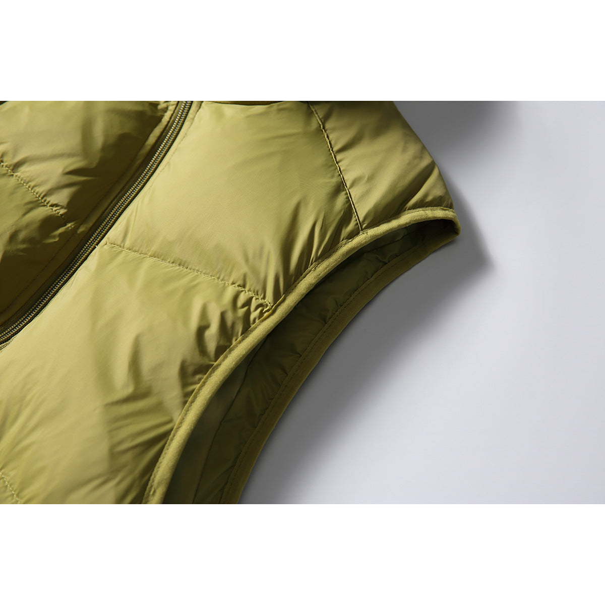 Close-up of the olive-green puffer vest armhole binding, quilted panels, and front zipper.