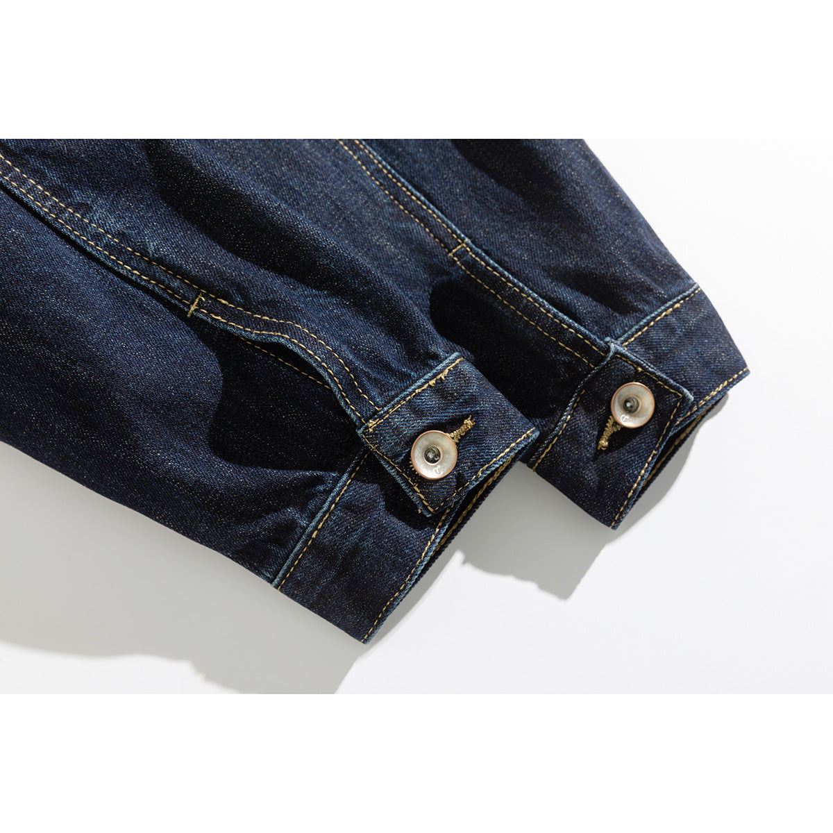 Close-up of two dark indigo denim jacket cuffs with buttons and golden contrast stitching.