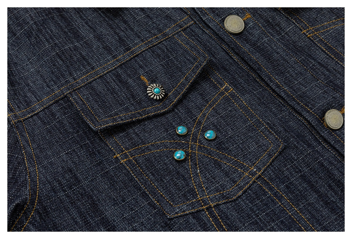 Close-up of dark indigo denim pockets with ochre stitching, metal buttons, and turquoise decorative accents.