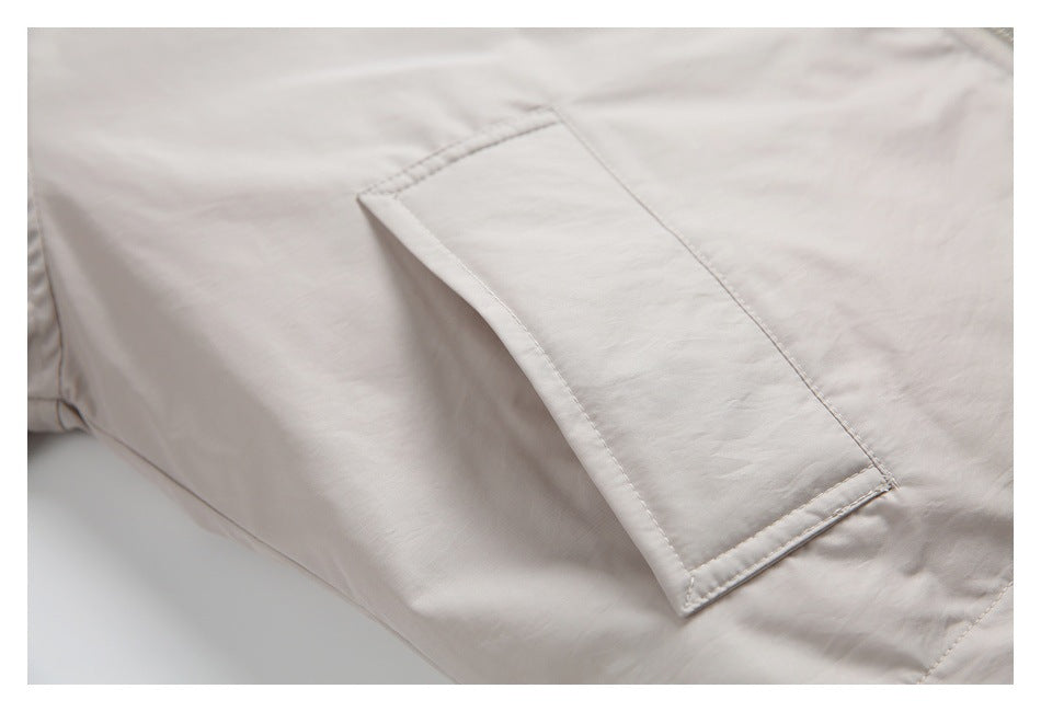 Close-up of a rectangular pocket stitched onto the light beige jacket.