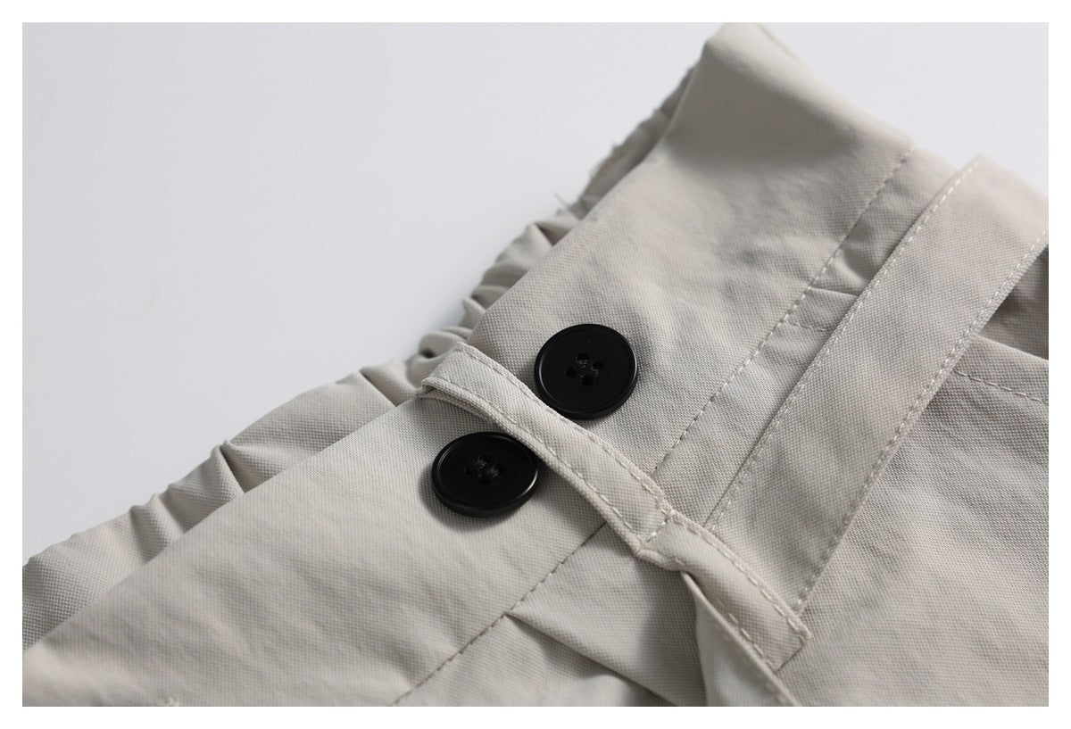 Close-up of a light taupe garment's waistband with two black buttons and a stitched fastening tab.