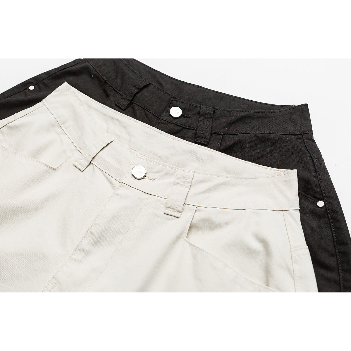 Close-up of cream and black shorts waistbands with belt loops, metal buttons and front pocket seams.