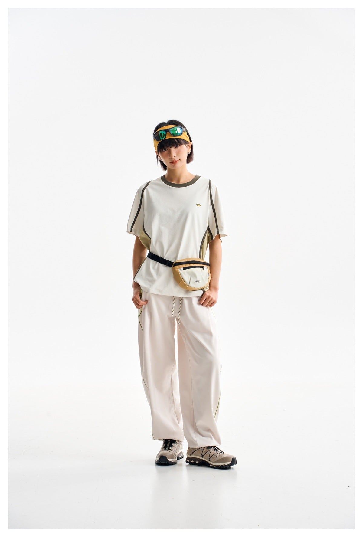 Front view of a model wearing an off-white piped T-shirt, loose white pants, and a tan waist bag.