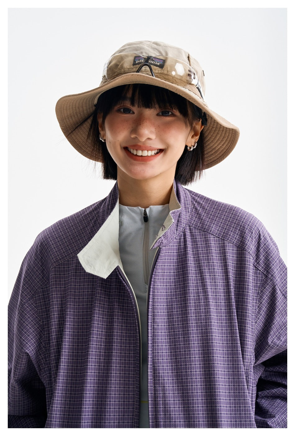 Close-up of a model wearing a purple plaid jacket with a pale contrasting collar and front zipper.