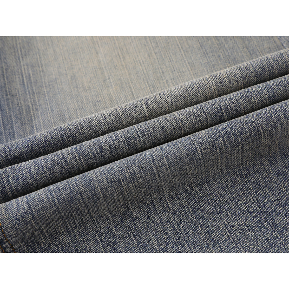 Close-up of blue-gray denim folded into ridges, showing its woven texture and washed finish.