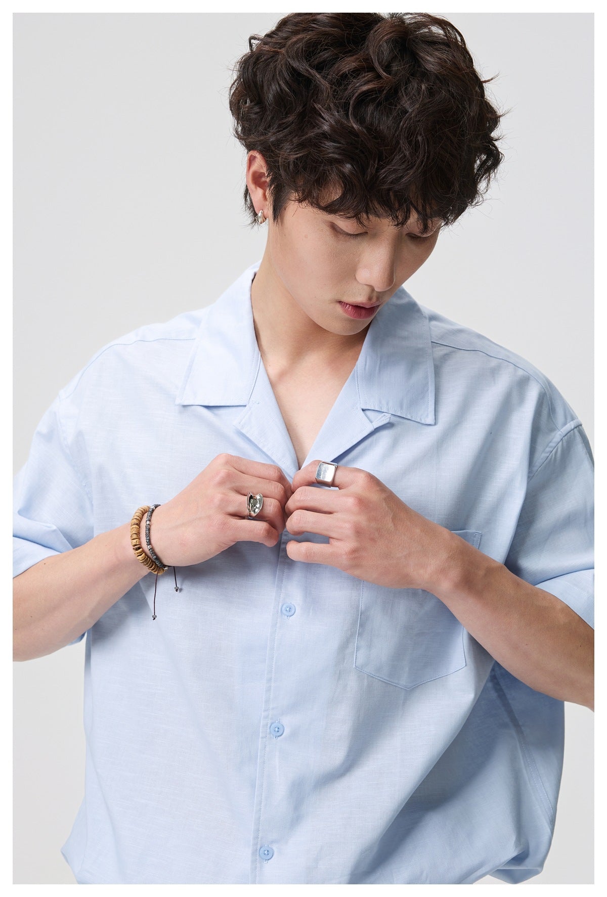 Male model wearing a pale blue short-sleeve button-up shirt with an open collar and chest pocket.