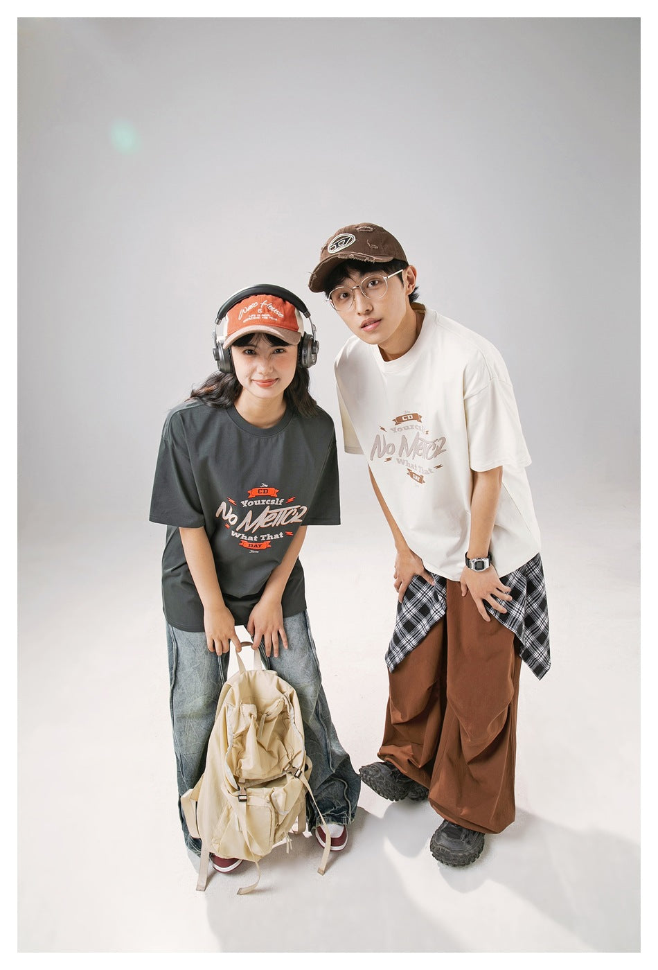 Two models lean forward in charcoal and off-white oversized T-shirts with front graphics.