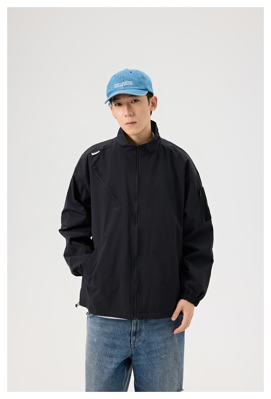 Model wearing a black zip-front jacket with a high collar, diagonal chest zipper and sleeve pocket.