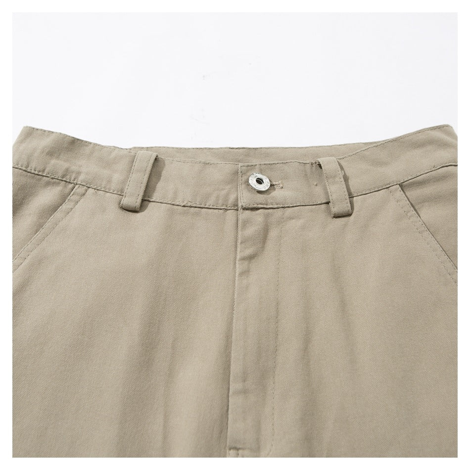 Close-up of beige pants at the waist, showing belt loops, a metal button, fly and angled pocket openings.