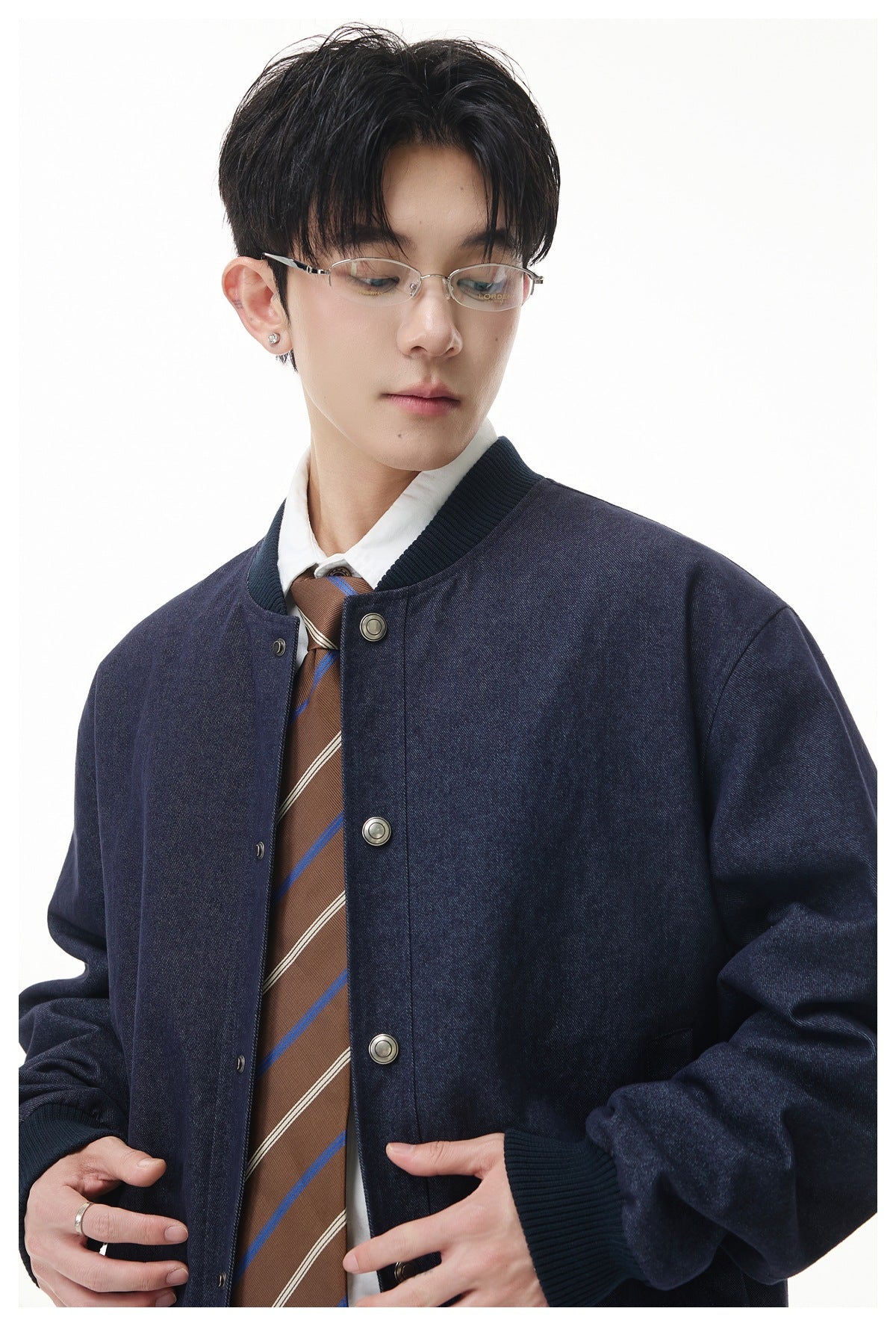 Model wearing a dark navy snap-front jacket with ribbed collar and cuffs over a white shirt and striped brown tie.
