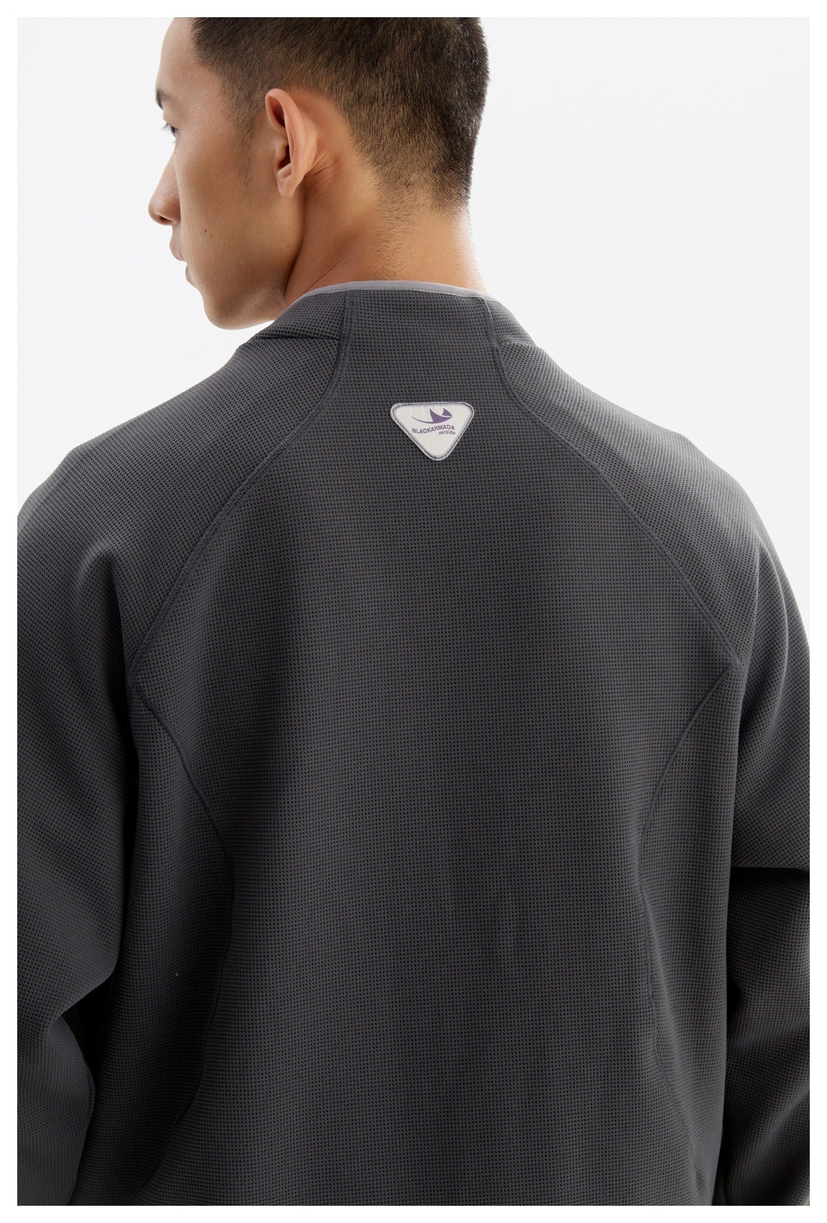 Close-up of a man wearing the back of a charcoal textured jacket with curved seams and a small triangular patch.
