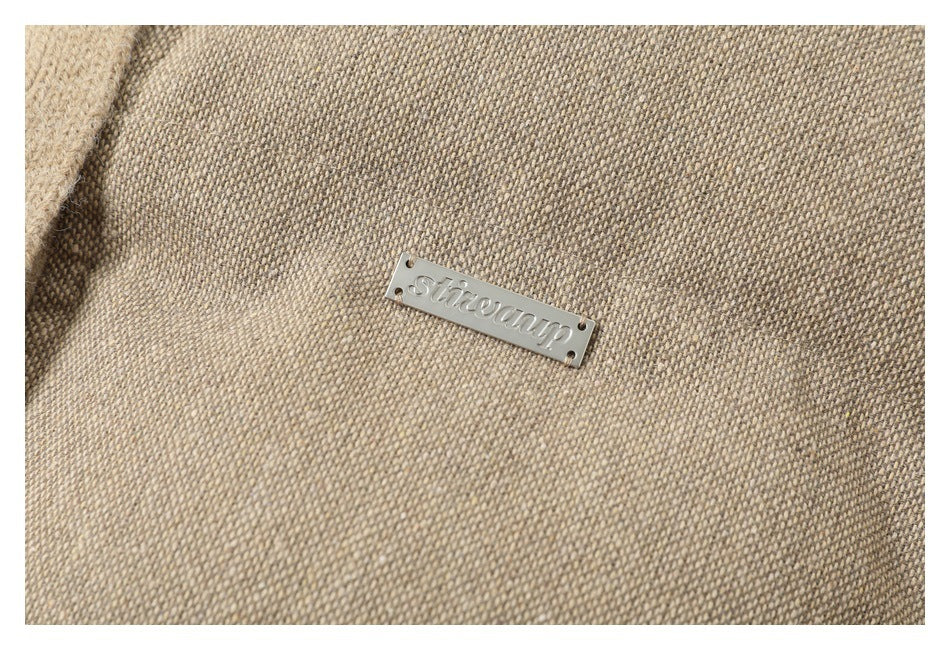 Close-up of the jacket's taupe woven fabric and a small silver-tone brand plate.