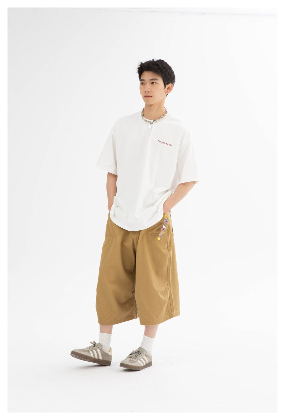 Model wearing loose khaki wide-leg knee-length shorts with a white T-shirt, chain necklace and gray sneakers