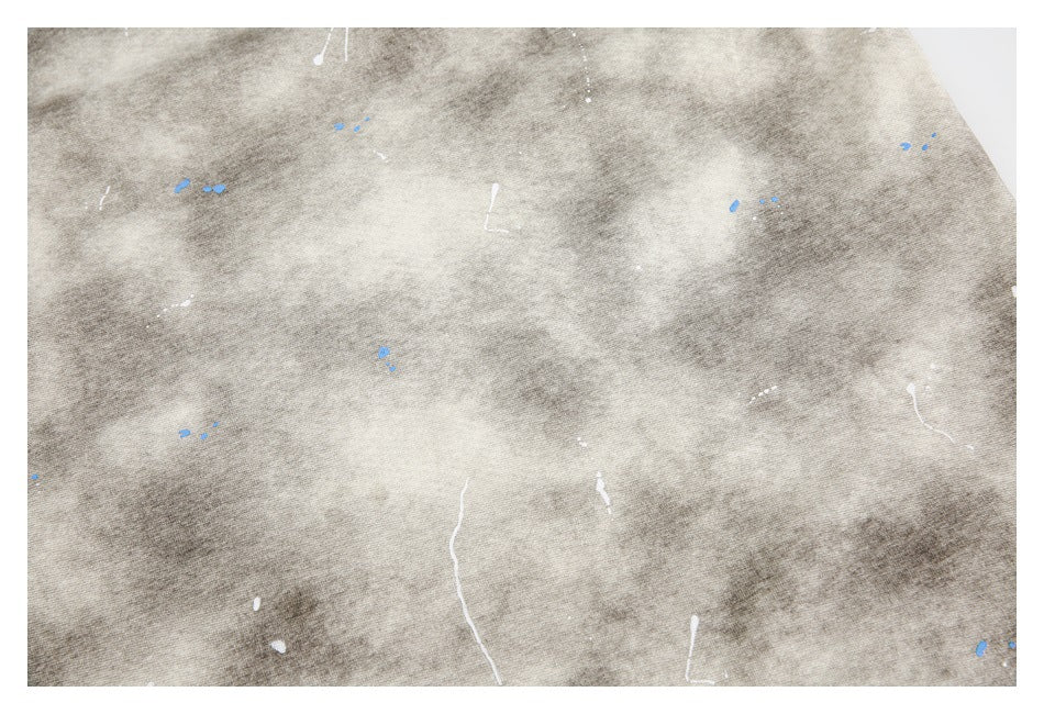 Close-up of gray-beige mottled fabric with scattered white and blue paint-like marks.
