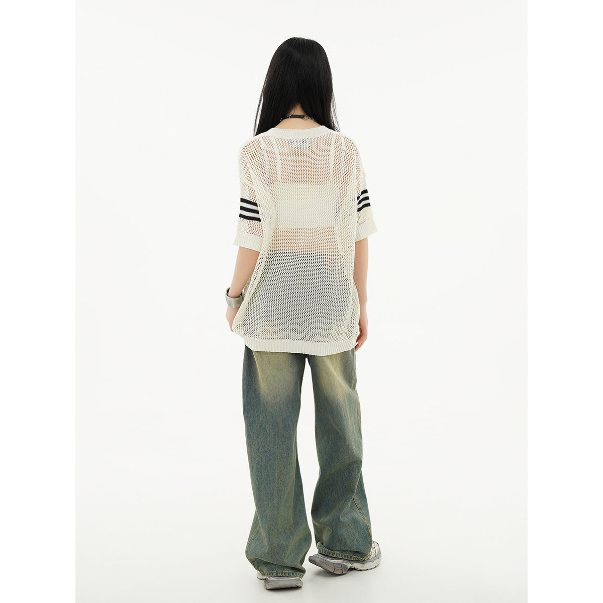 Back view of a model wearing an ivory open-knit tunic with black sleeve stripes and loose blue-green jeans.