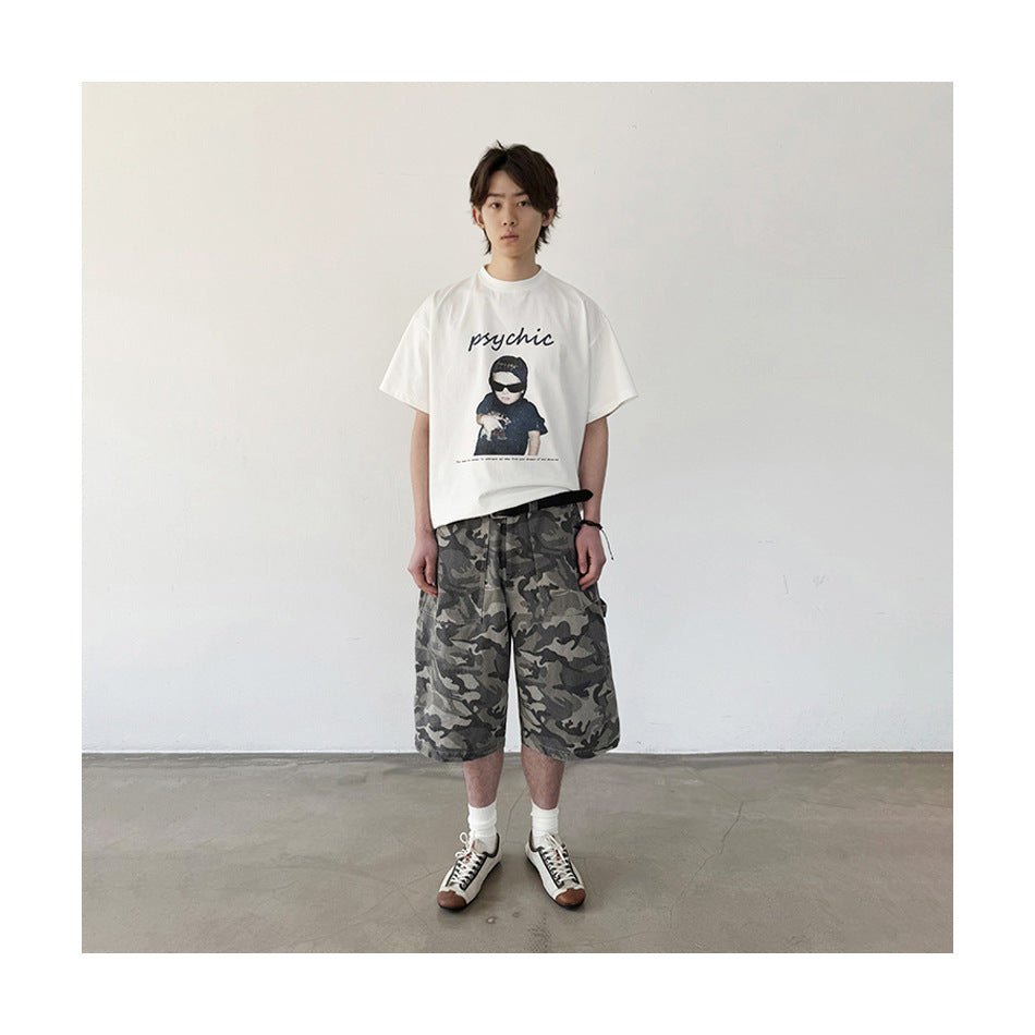 Full-length view of a person in camouflage knee-length shorts with a black belt, white graphic T-shirt and white socks