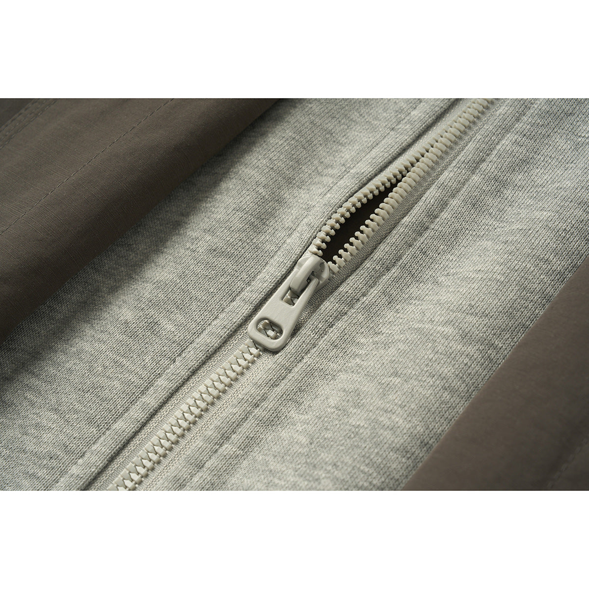 Close-up of a chunky light-colored zipper between the gray hood lining and dark brown jacket fabric.