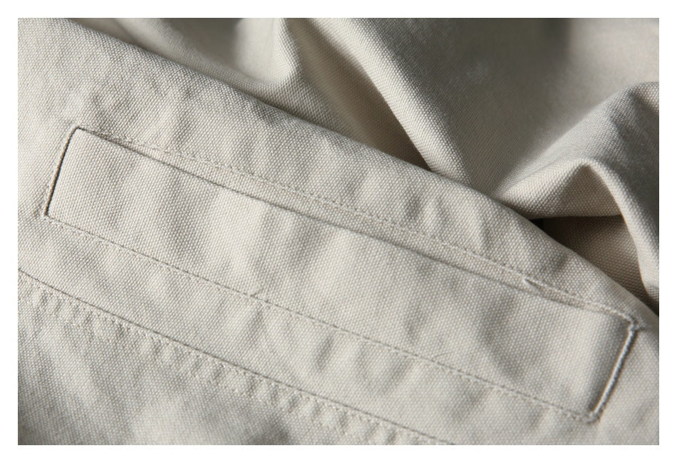 Close-up of a stitched rectangular pocket on light beige textured fabric.